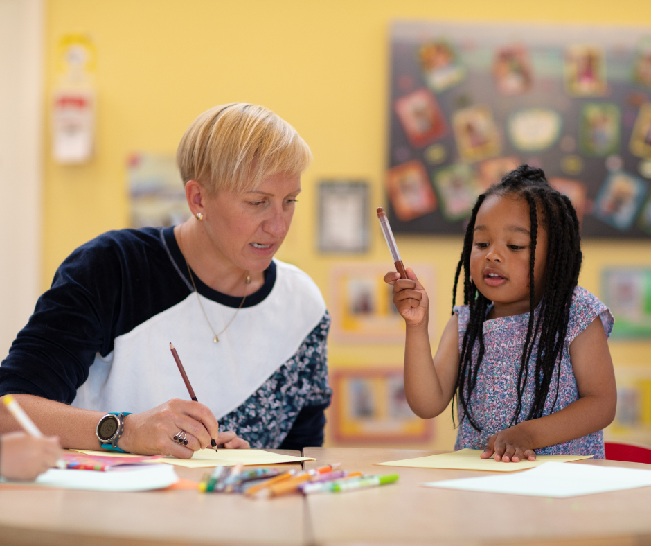 A woman and a young child sitting down at a table, drawing.